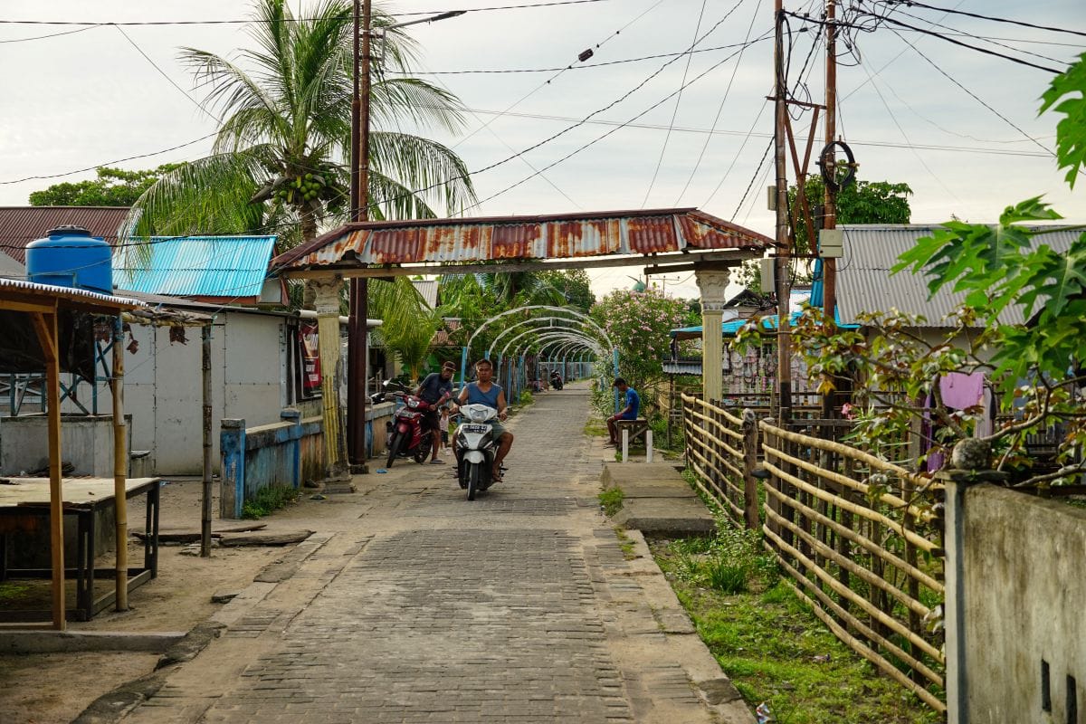Eine Straße auf Bunaken in Sulawesi mit einem Tor zum muslimischen Teil und einem Motorroller