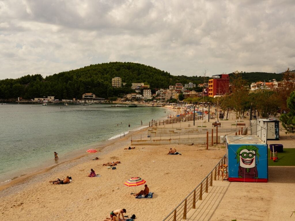 Public Beach, Öffentlicher Stadtstrand von Himara mit sanftem Wellengang und Blick auf die Küstenlinie.